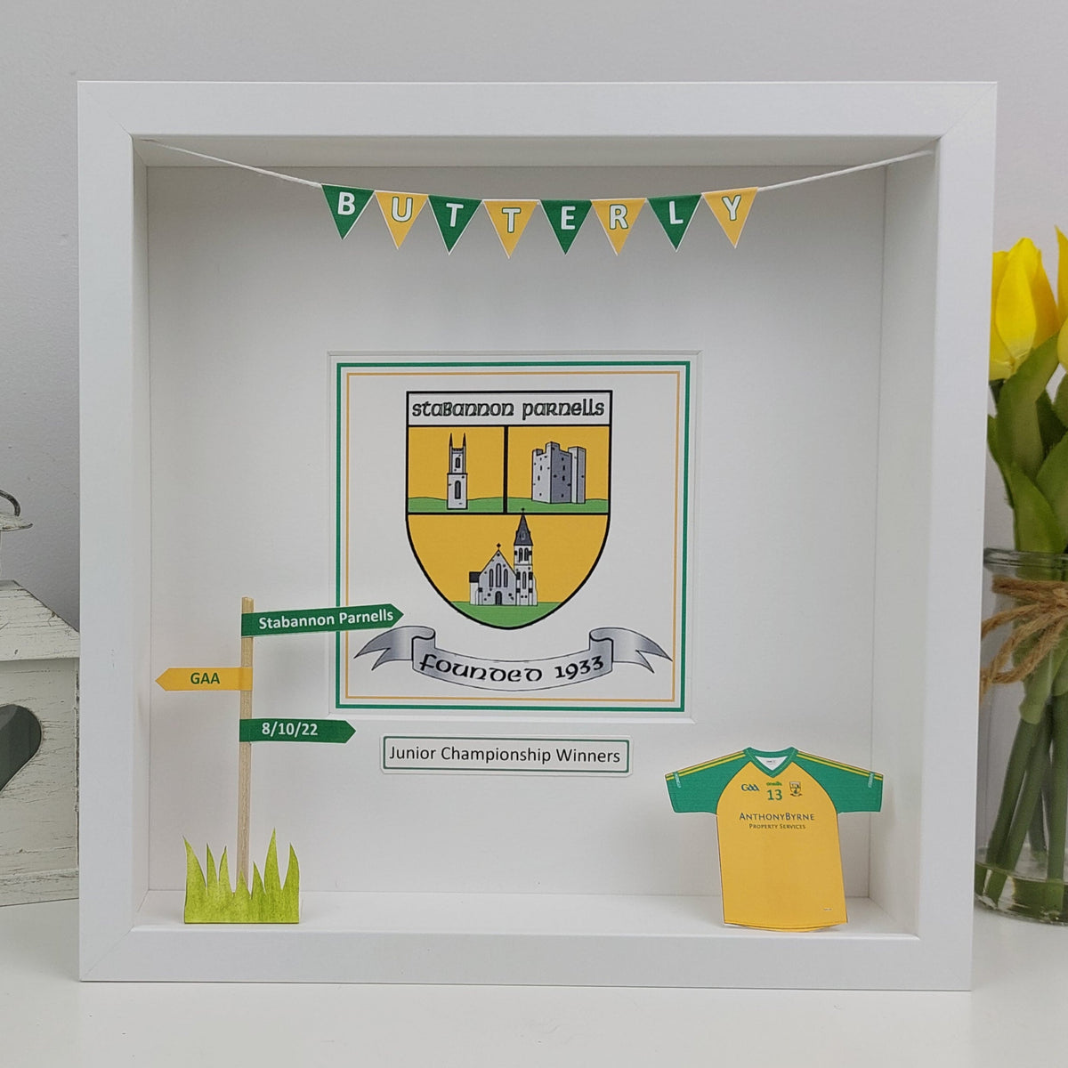 Decorative shadow box with a crest, flag, and jersey in a white frame.