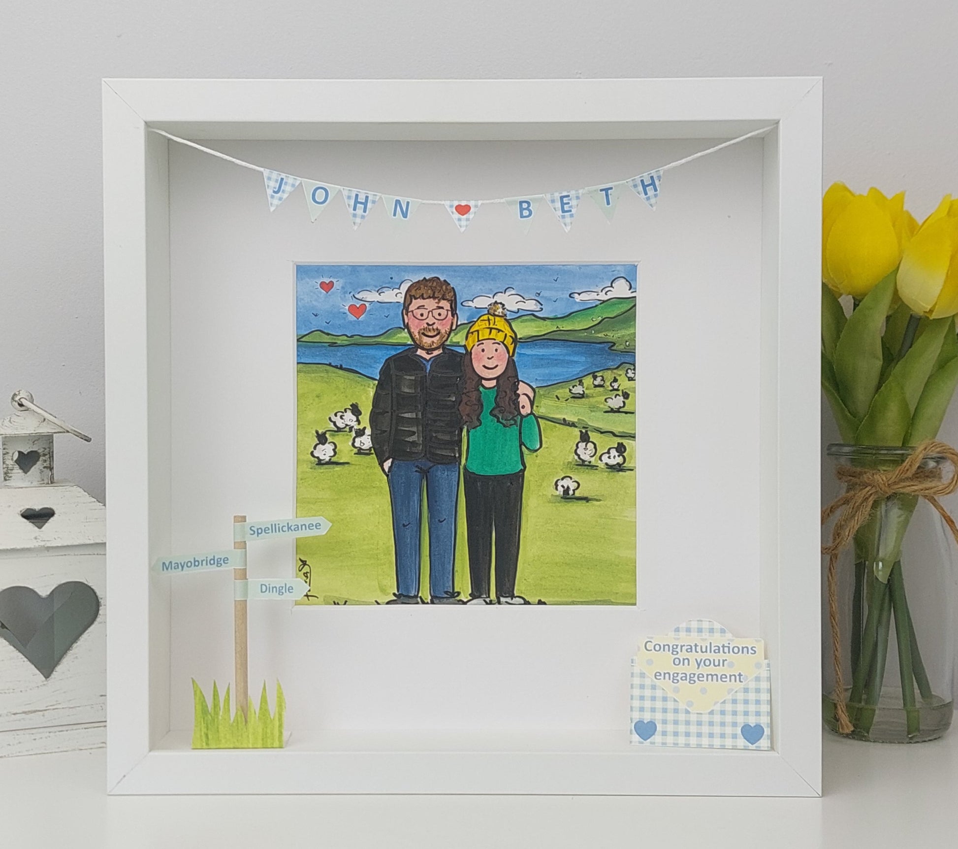 Framed artwork of a couple with a scenic background, displayed on a white surface with a vase of yellow tulips.