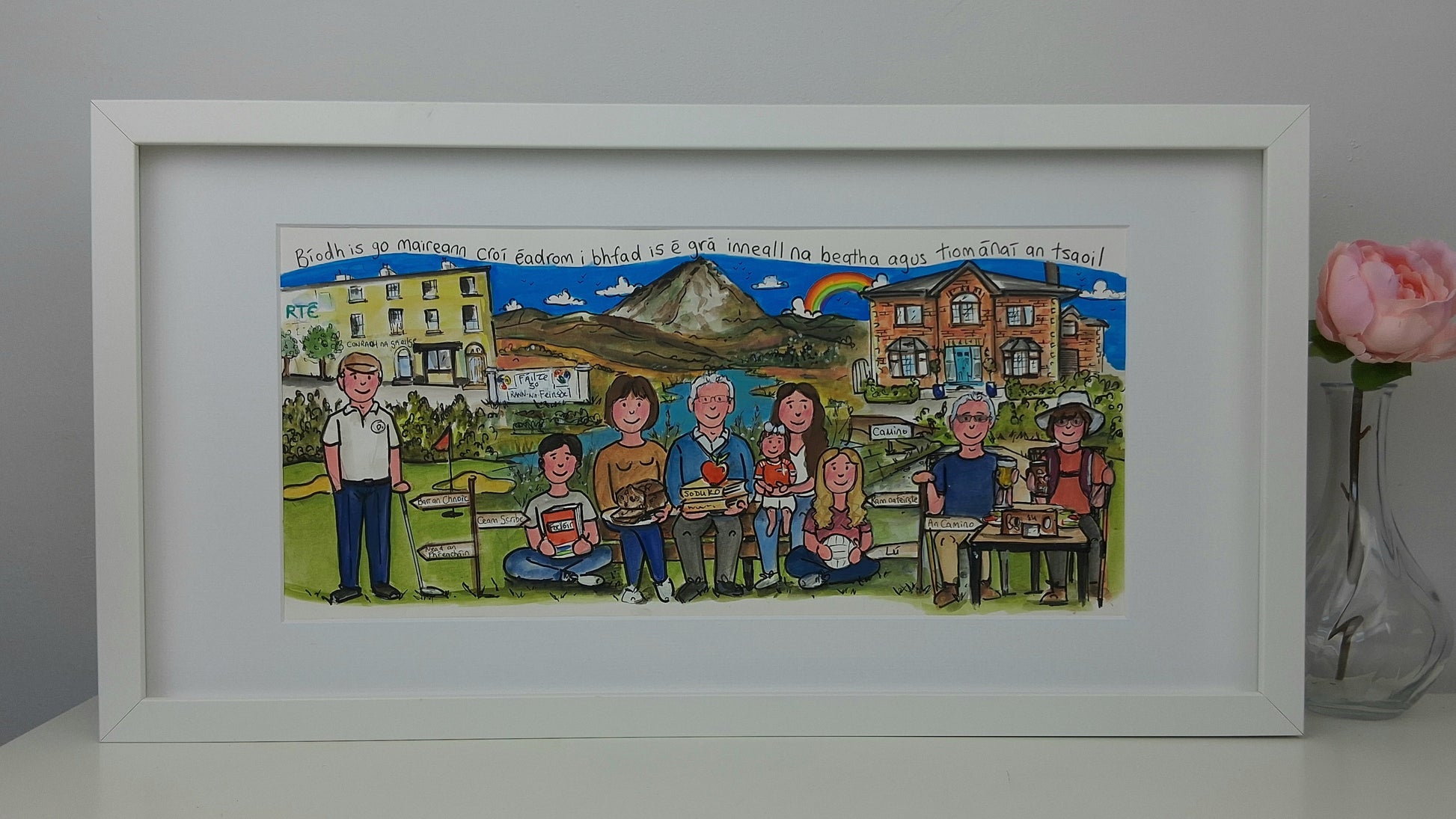Framed artwork of a family scene with a scenic background, placed on a white surface.