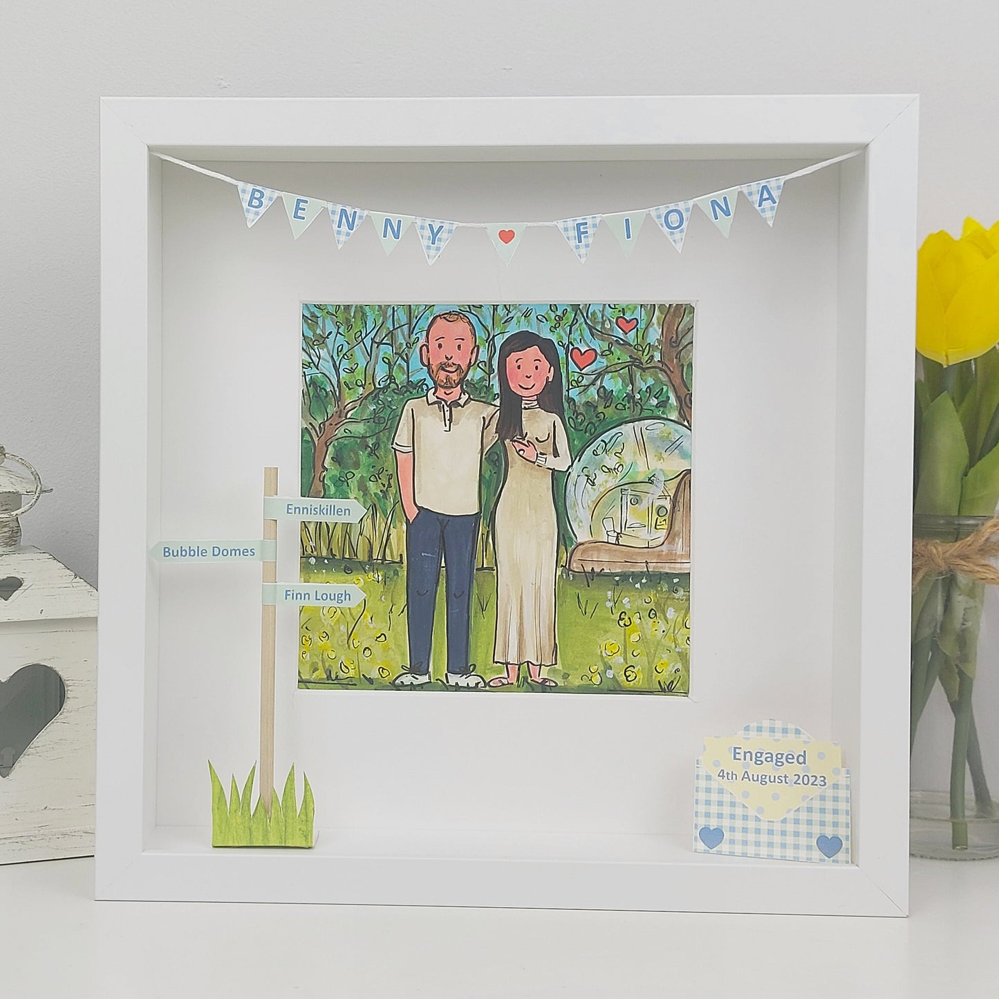 Framed illustration of a couples engagement with personalized details on a white surface.