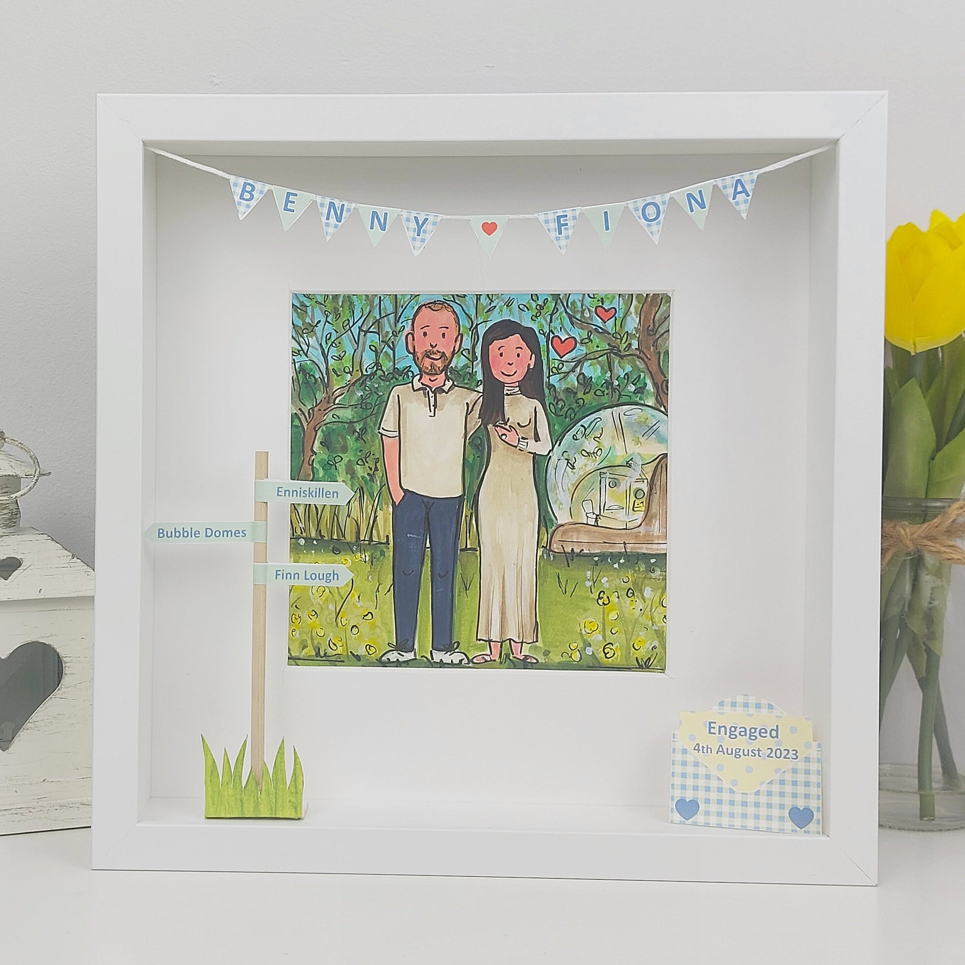 Framed illustration of a couples engagement with personalized details on a white surface.
