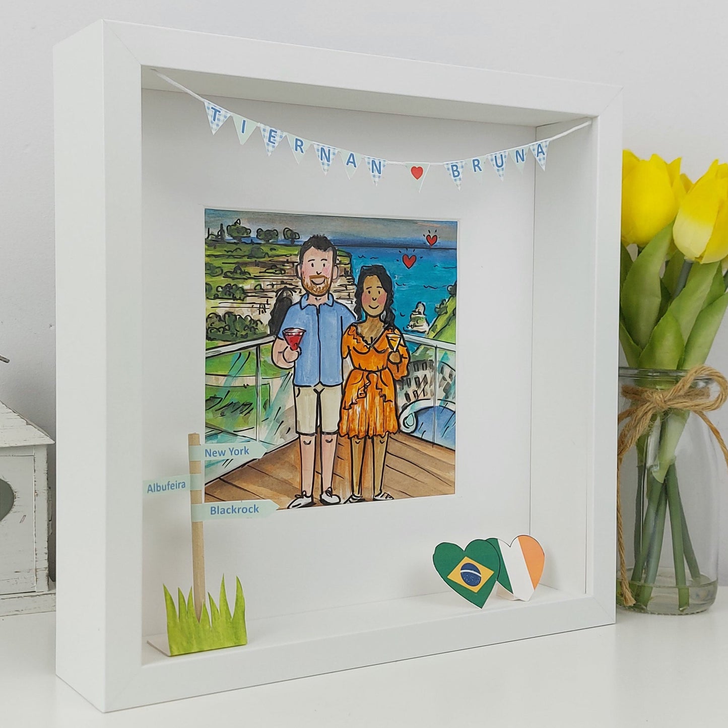 White shadow box with a illustration of a couple, small flag, and yellow tulips on a white background