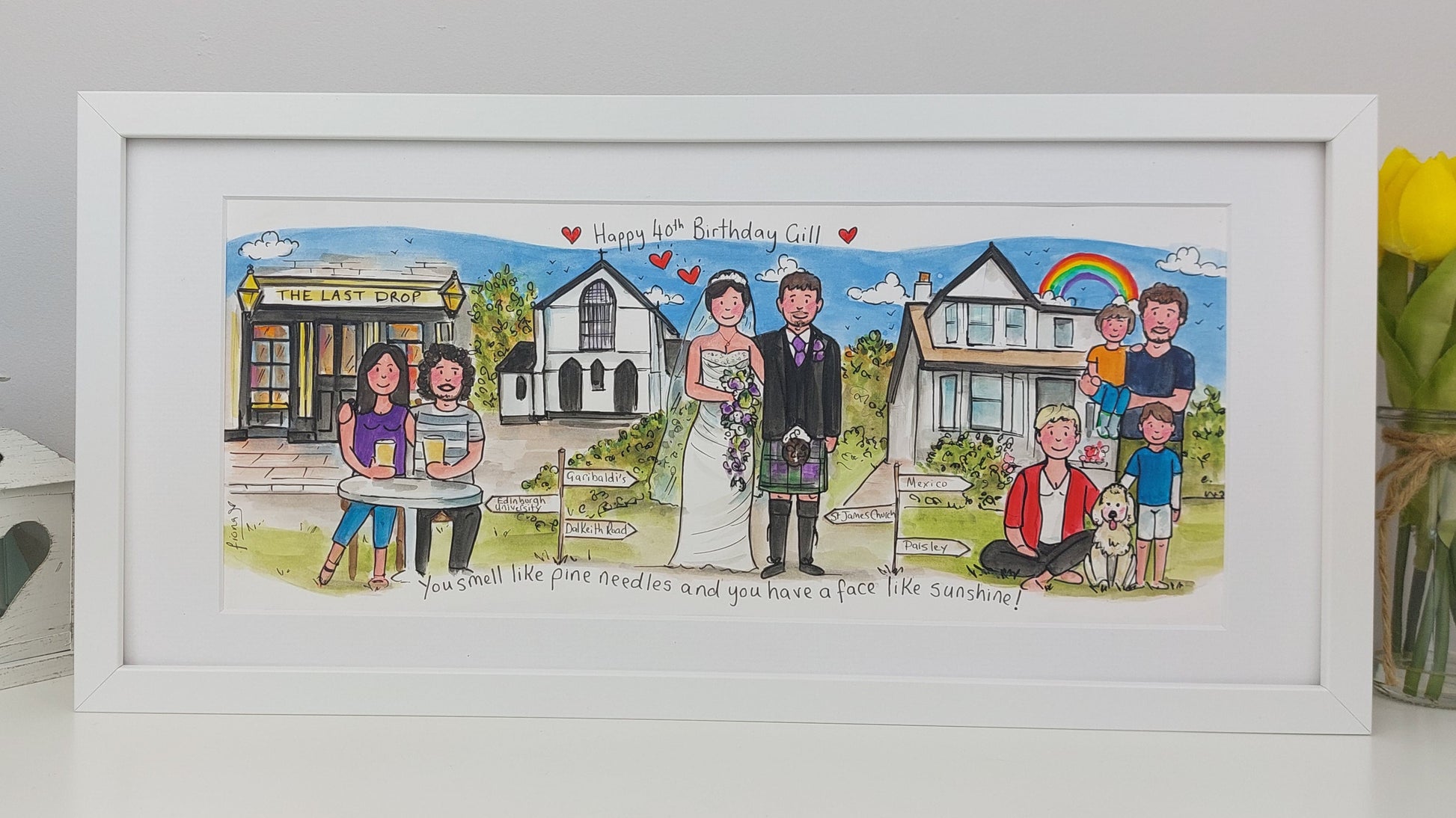 Framed artwork of a wedding scene with people and buildings, on a white surface with a vase of flowers.