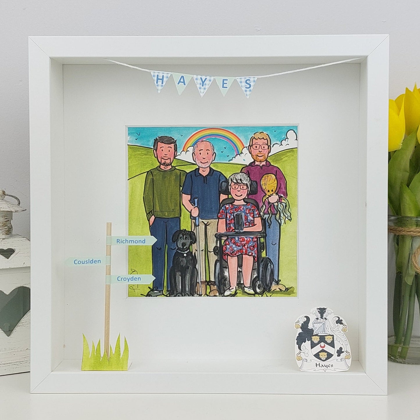 Framed illustration of a family with a rainbow, flowers, and a coat of arms on a white surface.