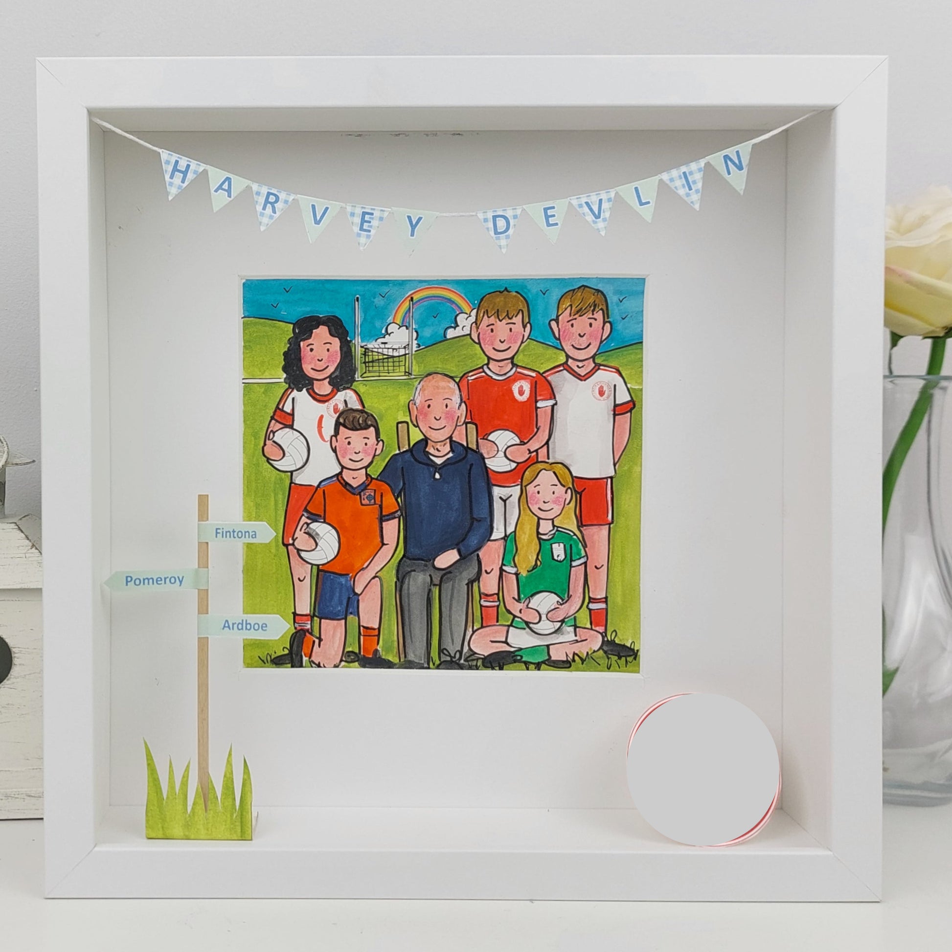 Framed illustration of a family on a sports field with a banner above, on a white surface.