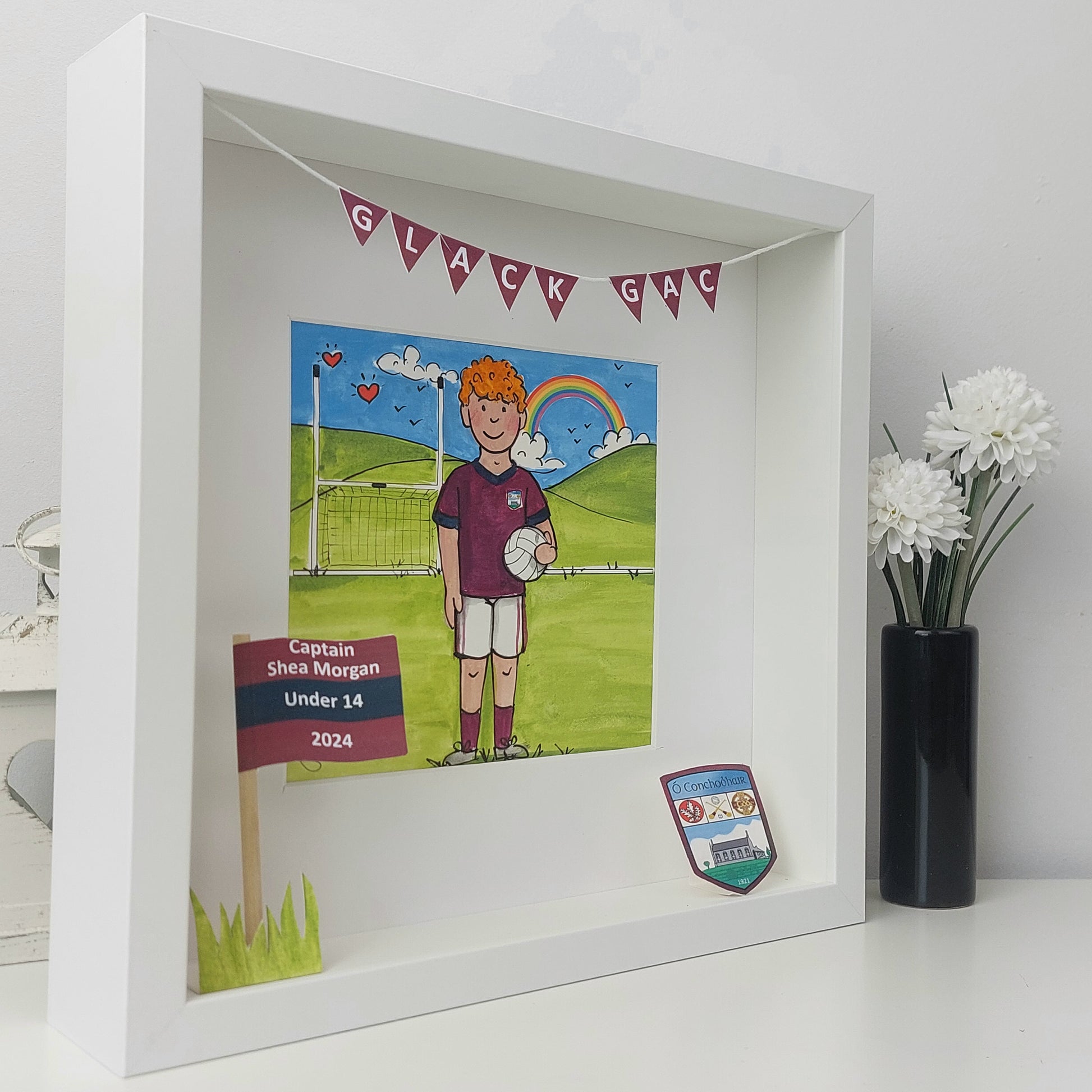 Framed artwork of a boy playing gaelic football with decorative elements on a white surface.