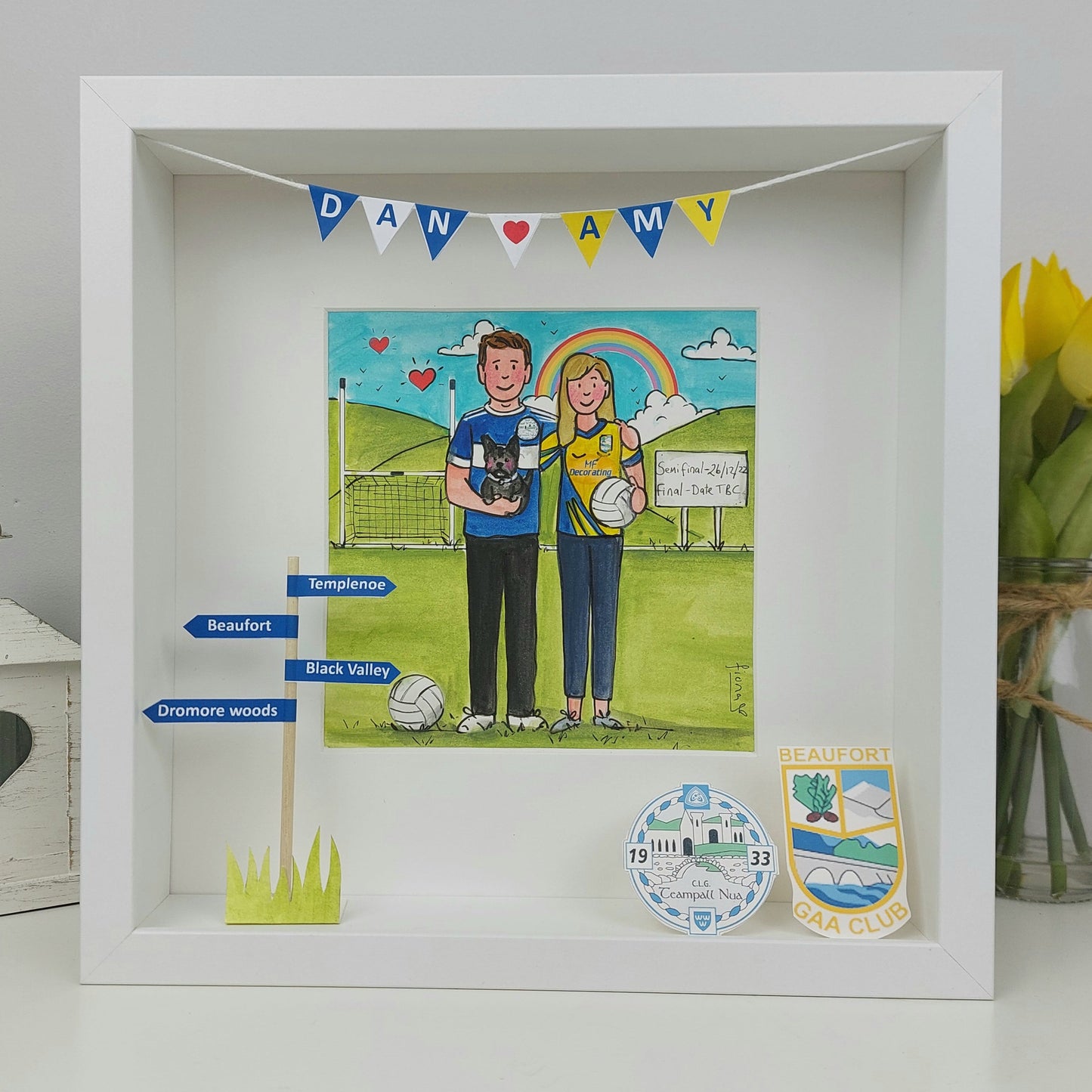Decorative shadow box with a illustration of two people, a rainbow, and small flags on a white background.