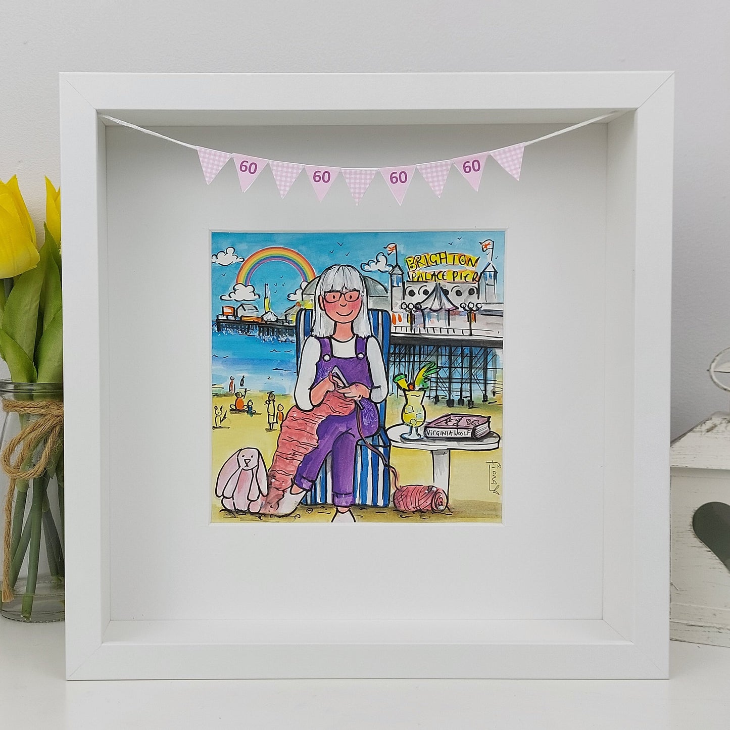 Framed artwork of a woman sitting on a beach with a rainbow and '60' banner above her.