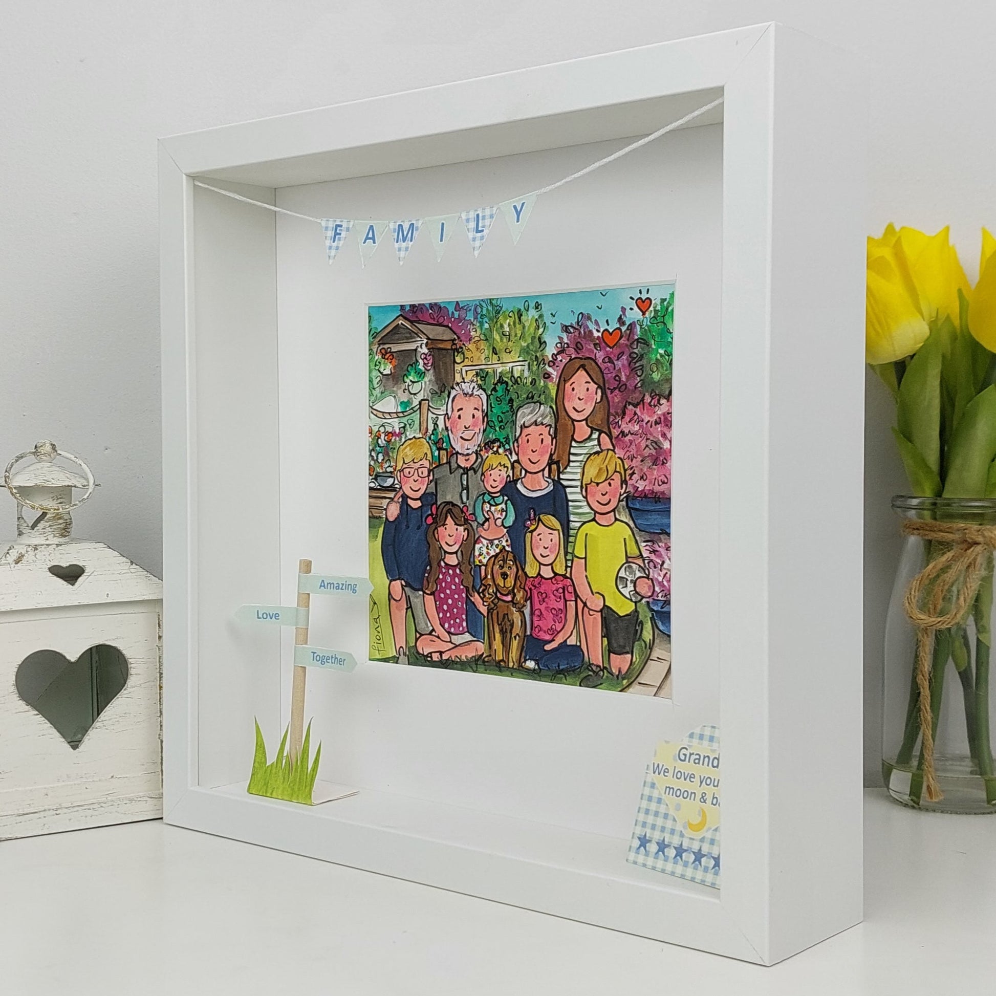 White shadow box with a colorful family illustration, decorative elements, and a vase of yellow tulips.