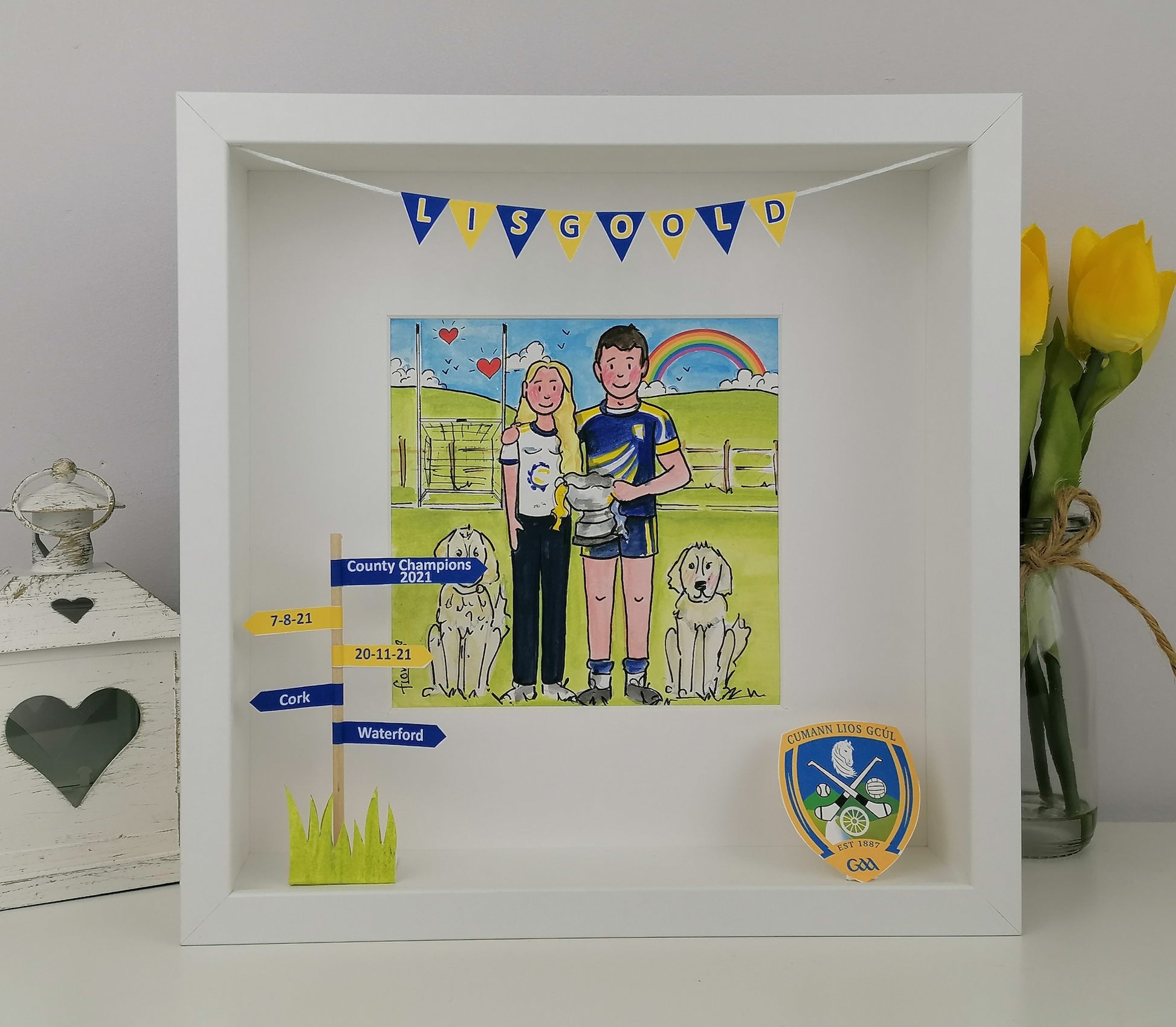 Framed artwork with a gaelic hurling couple and dogs, celebrating achievements, on a white surface with decorative items.