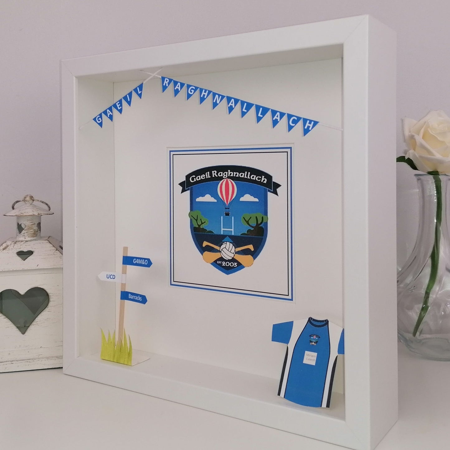 Decorative shadow box with a crest, flags, and a sports jersey on a light background.