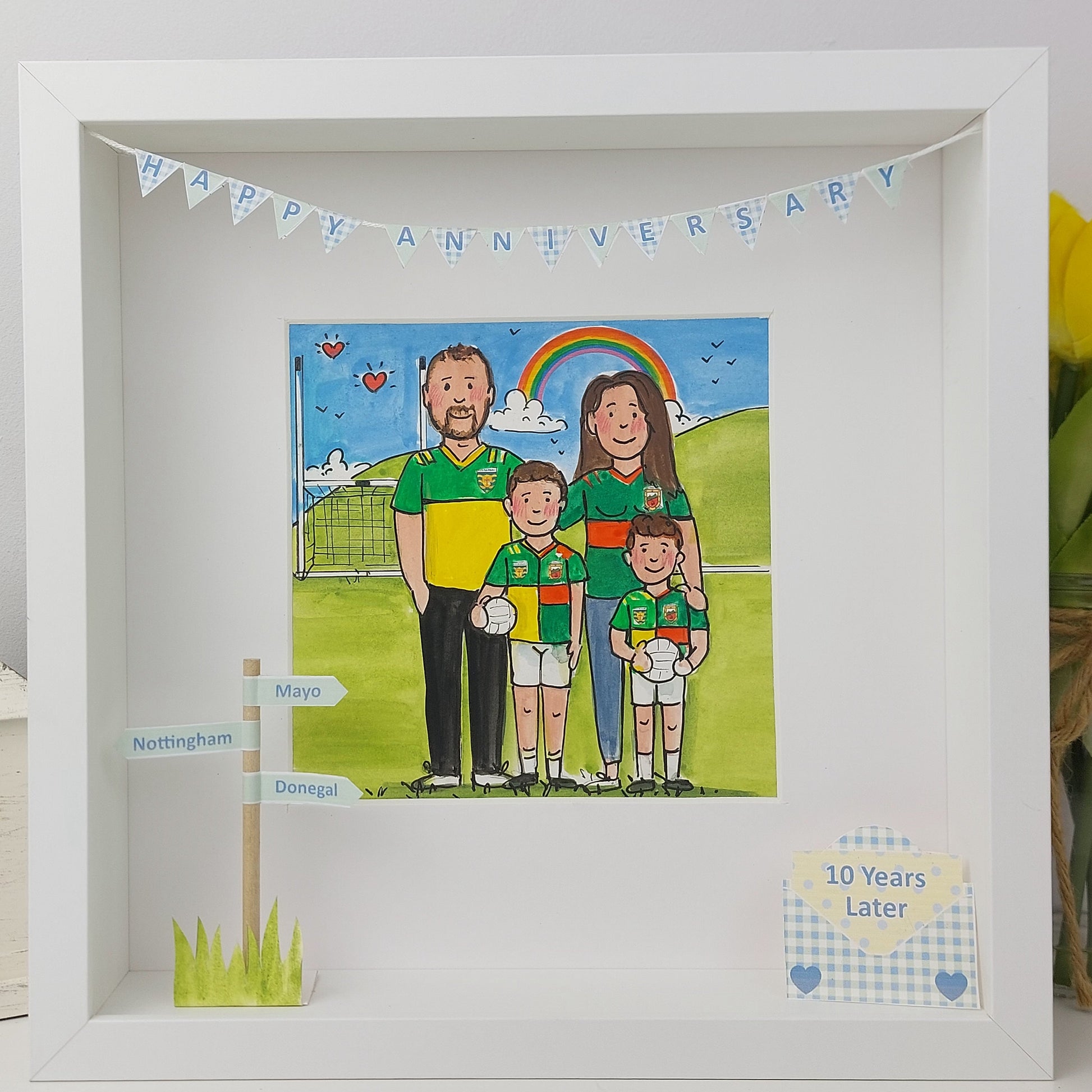 Framed artwork of a gaelic football family at a sports event with decorative elements.