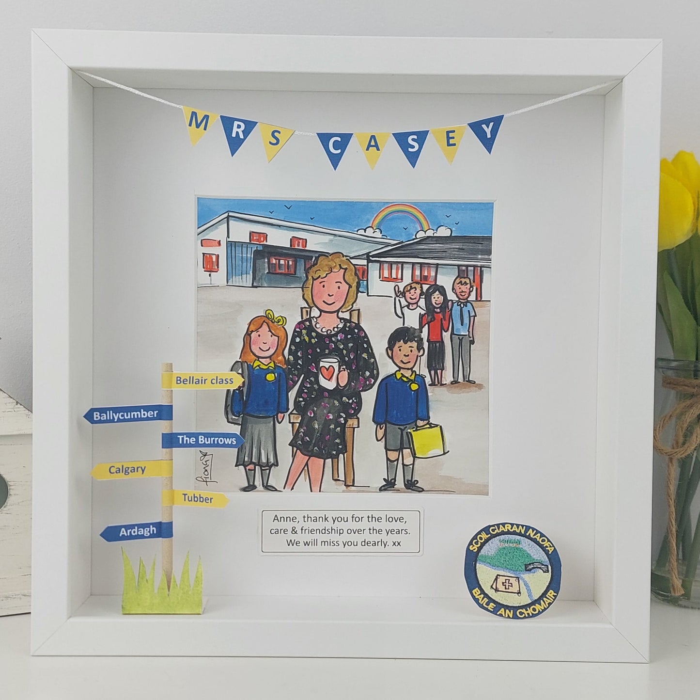 Framed picture of a teacher and students with a 'Mrs Casey' banner, next to a vase of yellow tulips.