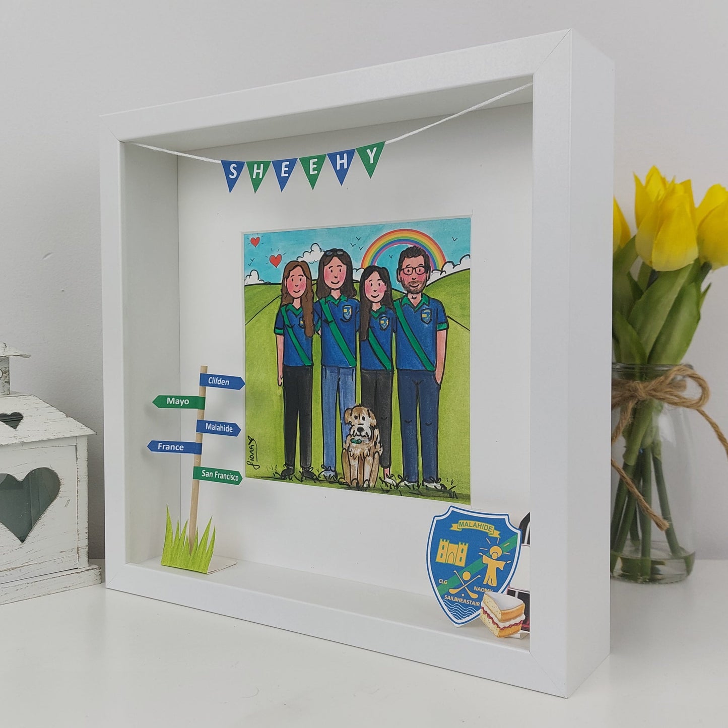 Framed artwork of a family with a dog, surrounded by decorative elements on a white surface.