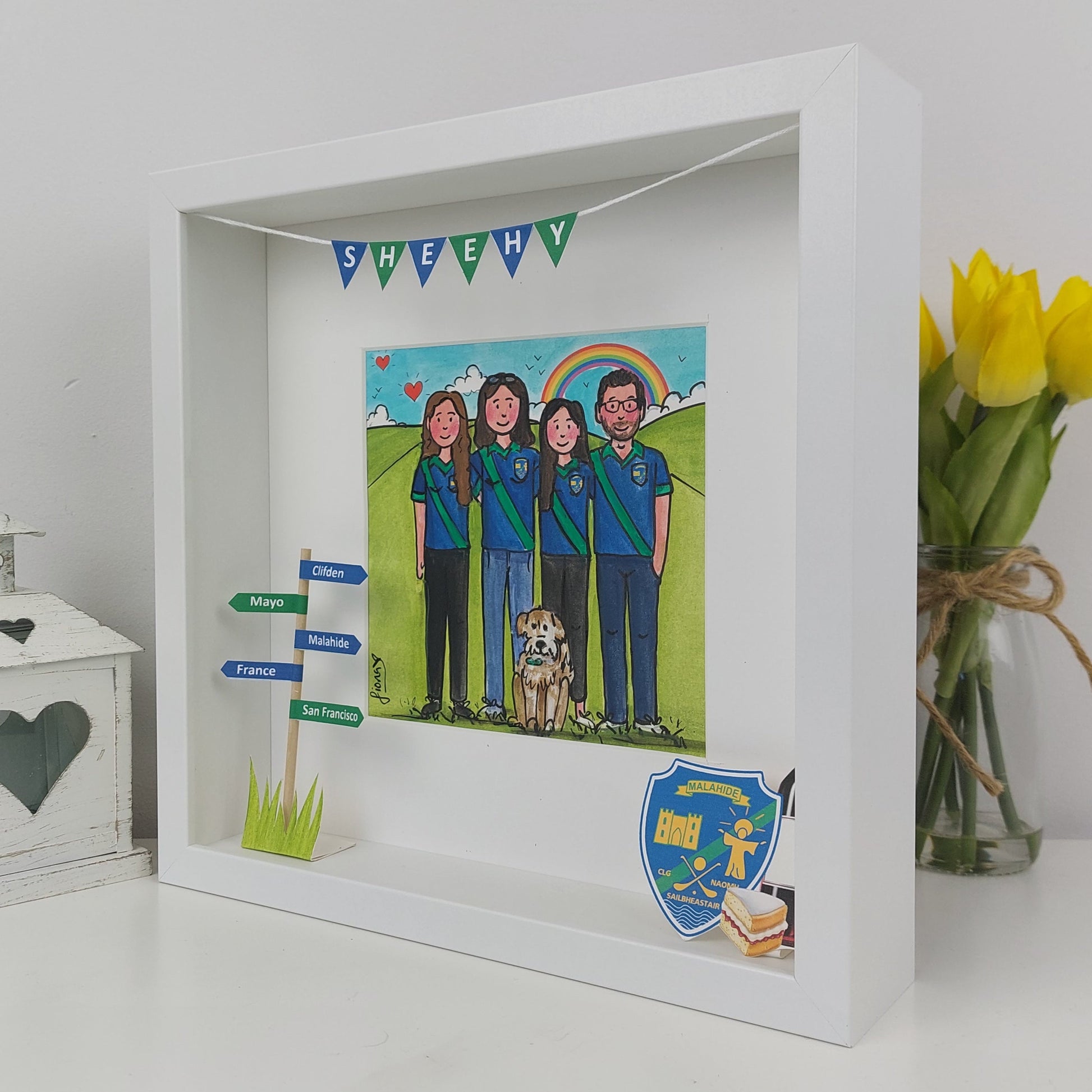 Framed artwork of a family with a dog, surrounded by decorative elements on a white surface.