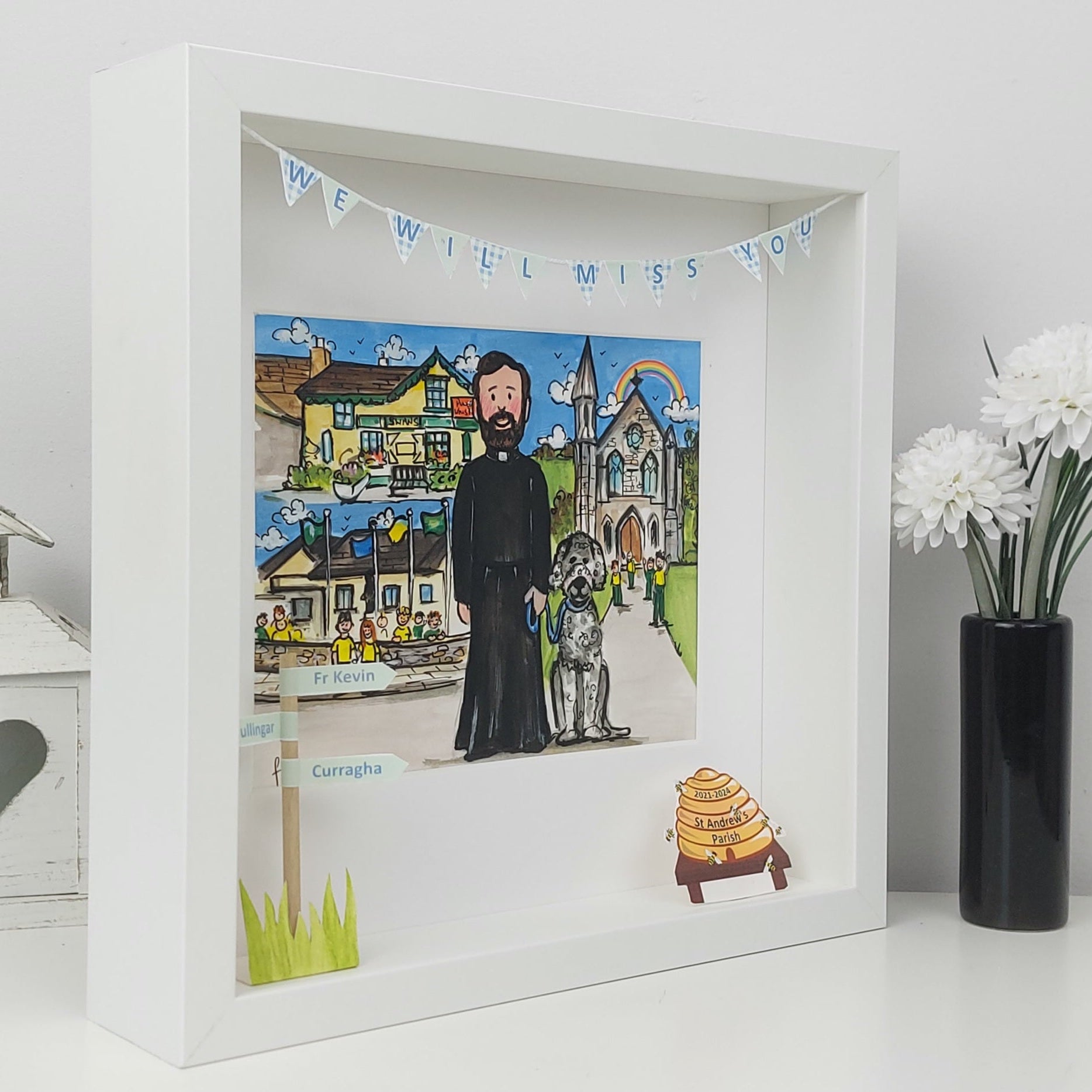 Framed artwork with a priest and church scene, featuring a small banner above.