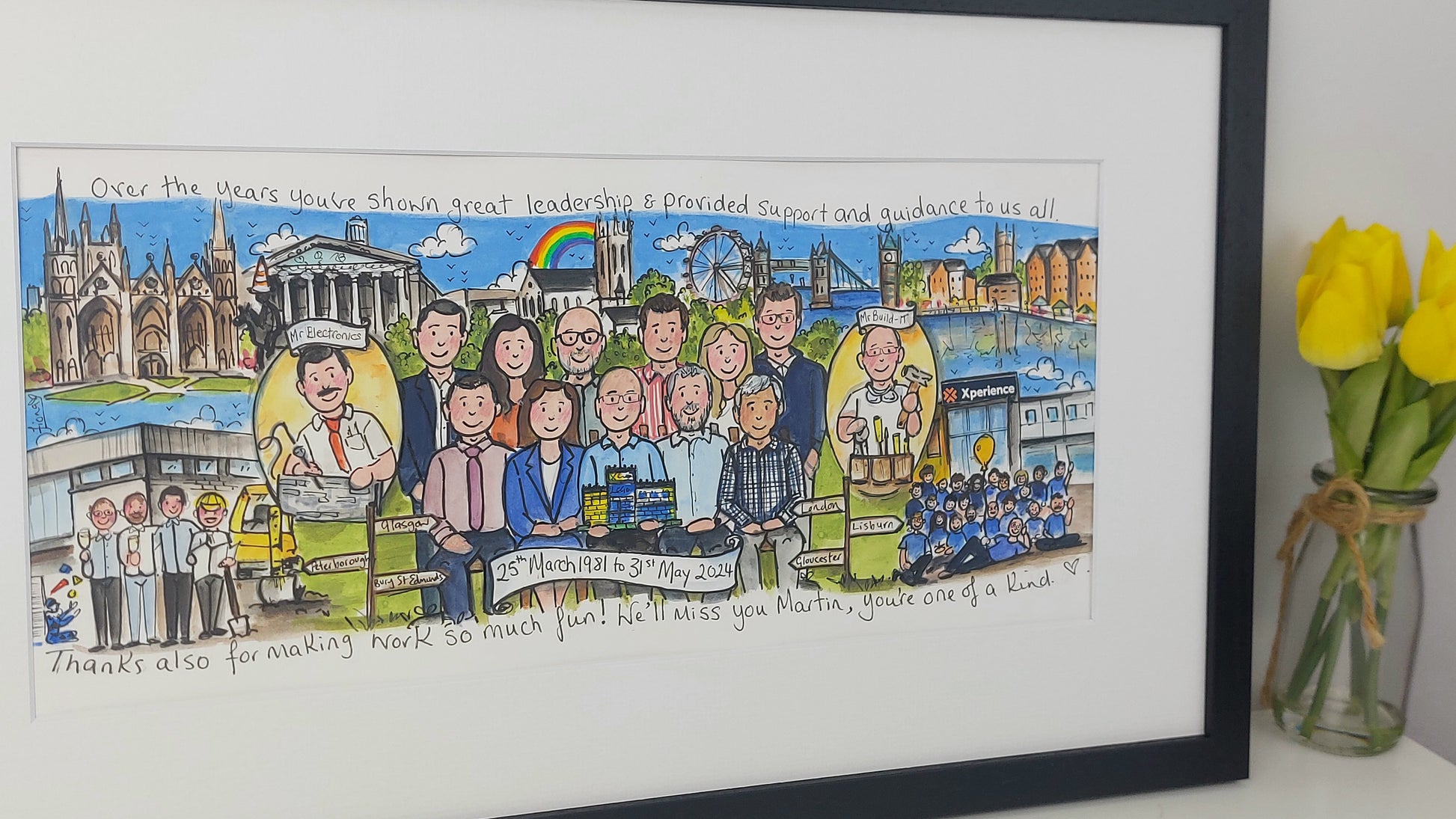 Framed artwork with a colorful illustration of people and landmarks, featuring a vase of yellow tulips on a white surface.