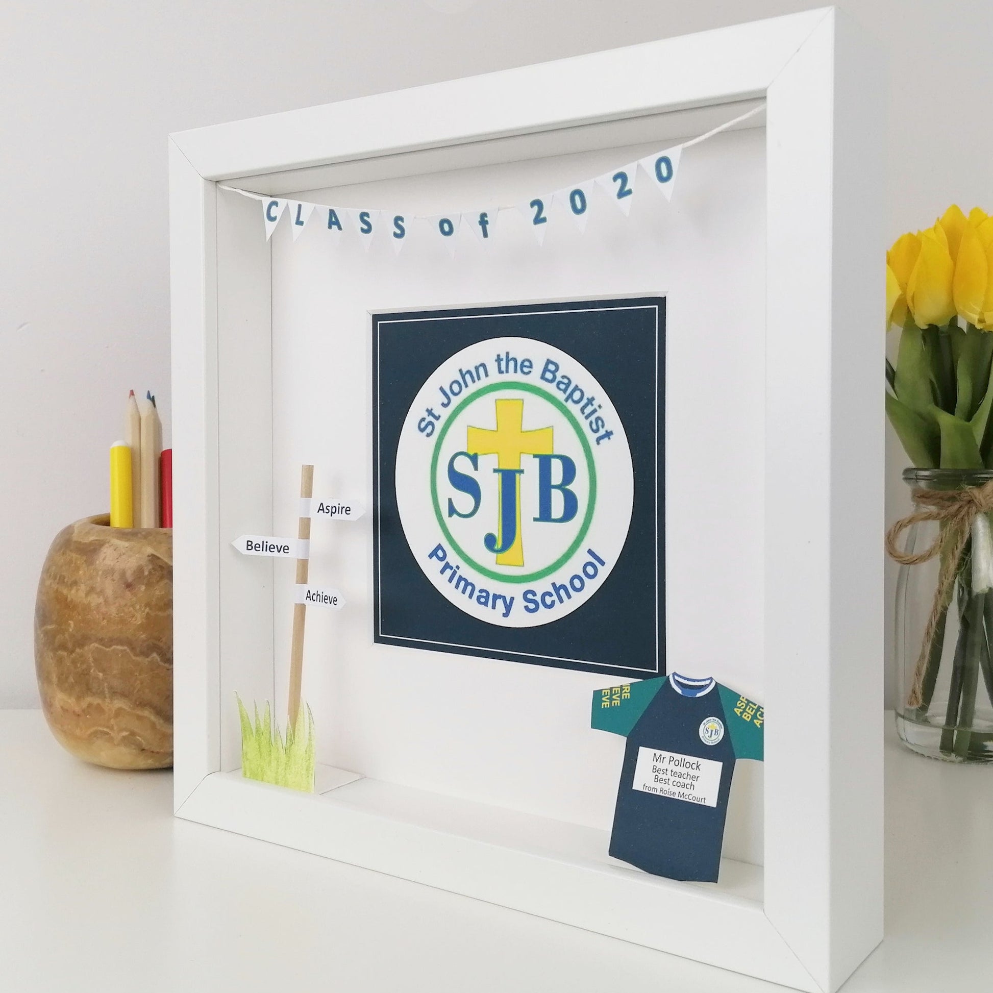 Framed display with St John the Baptist Primary School logo and school uniform cutout on a white surface.
