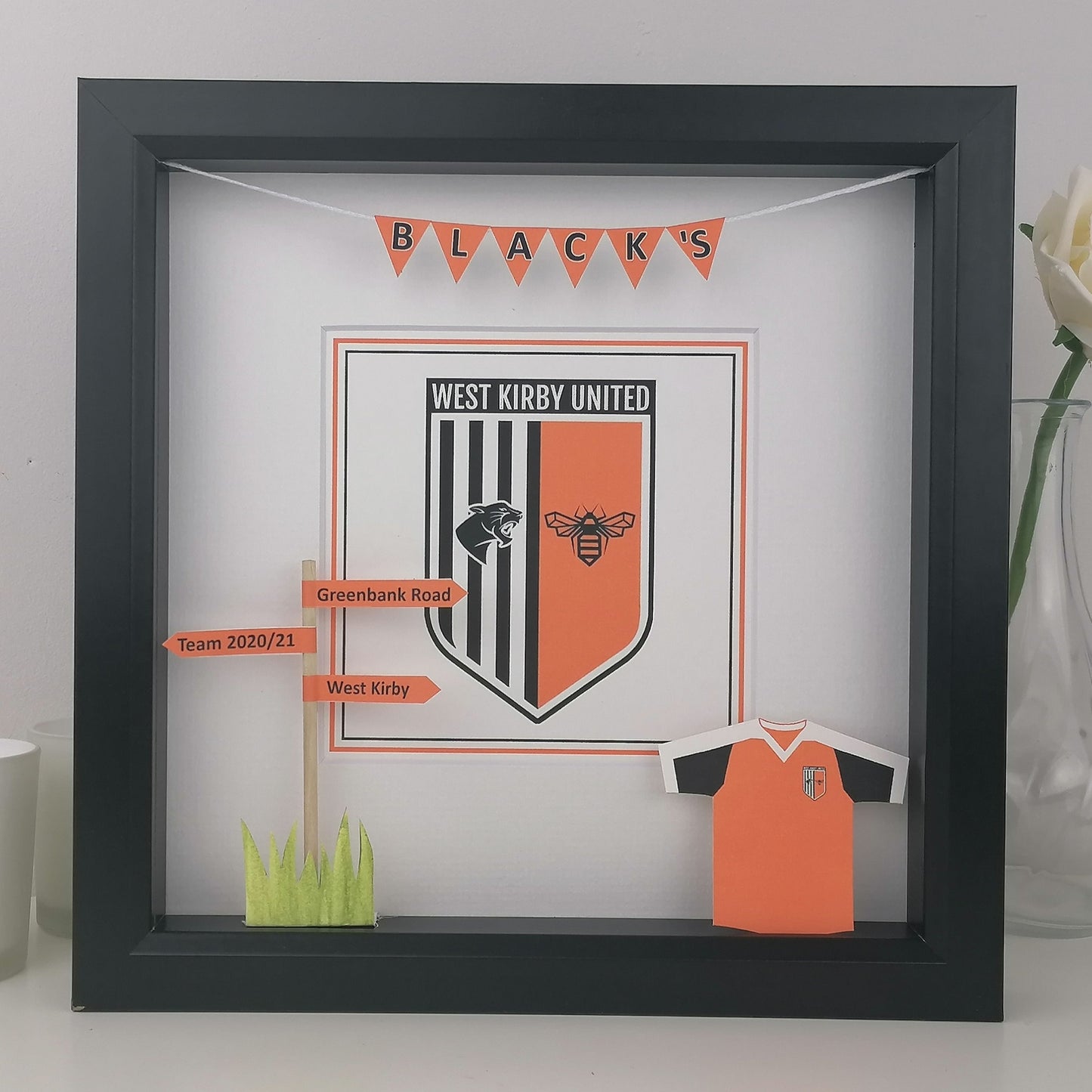 Framed display of West Kirby United football club merchandise with a black frame.