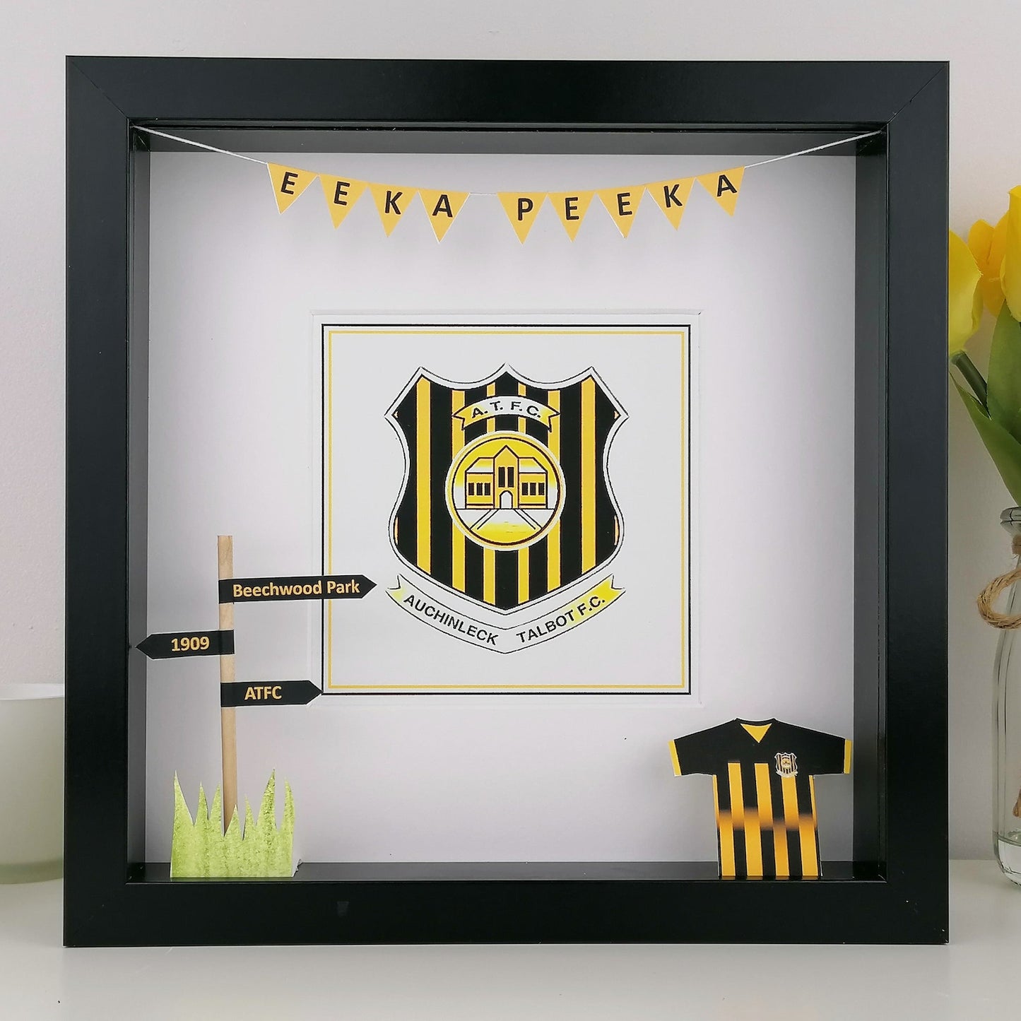 Framed sports team logo with yellow and black colors, placed on a white surface.