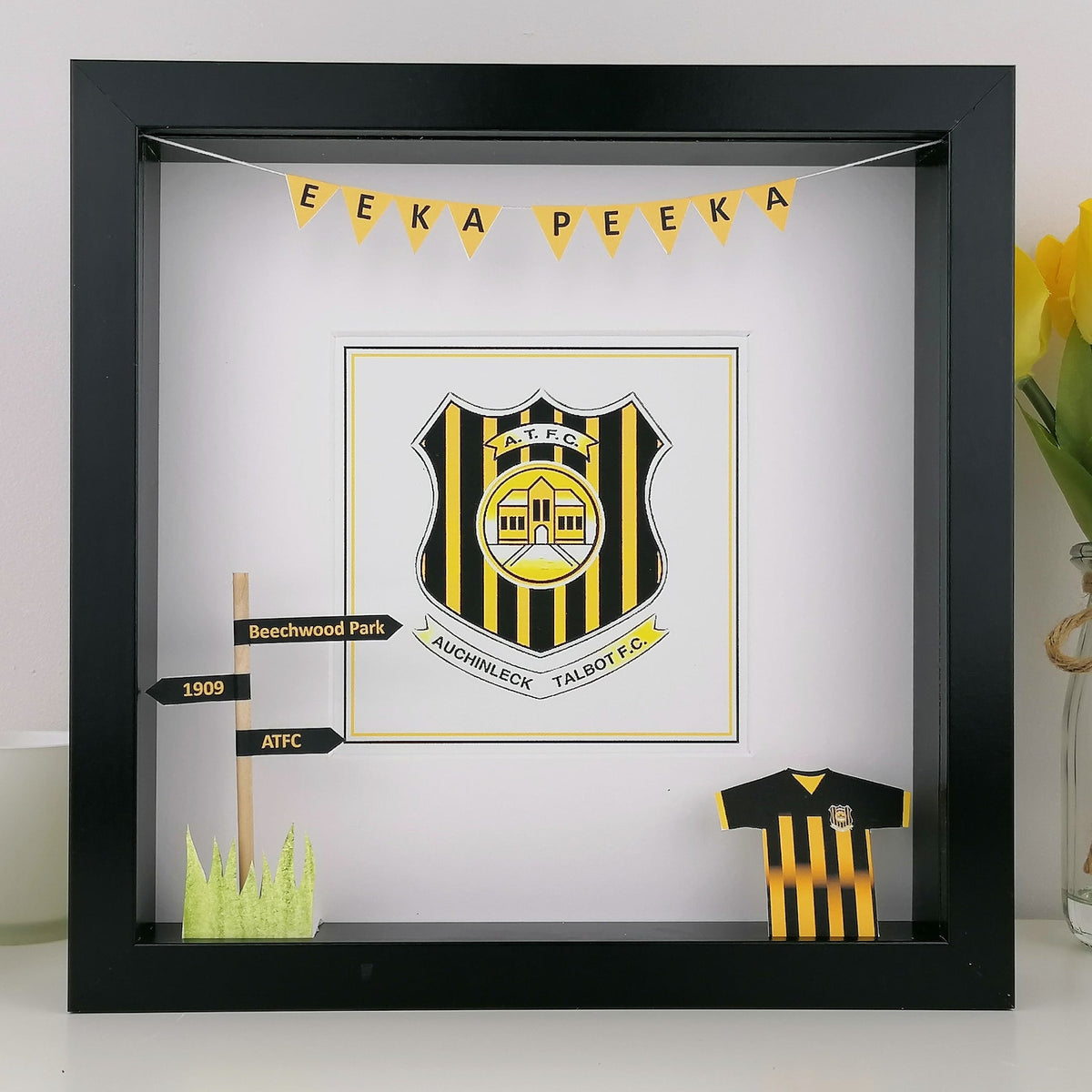 Framed sports team logo with yellow and black colors, placed on a white surface.
